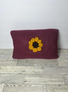 a crocheted bag with a yellow flower on the front and purple bottom, sitting on a wood floor