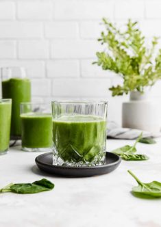 a glass filled with green liquid sitting on top of a table next to other glasses