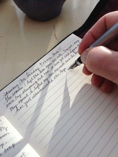 a person writing on lined paper with a pen in their left hand and another note pad next to them