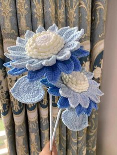 a person is holding some kind of blue and white crocheted flower on a stick