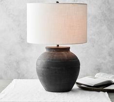 a table lamp sitting next to an open book on top of a white cloth covered surface