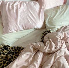 an unmade bed with pink sheets and leopard print pillows