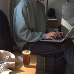 a man sitting in front of a laptop computer on top of a wooden table next to a cup of coffee