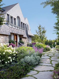 a stone path leads to a house with flowers in the foreground and bushes on either side