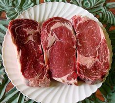 three pieces of raw meat on a paper plate with green leaves in the background,