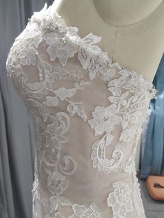 the back of a wedding dress with white lace and flowers on it, sitting on a mannequin