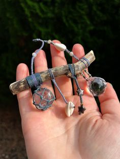 a hand holding a piece of wood with beads and charms on it's end