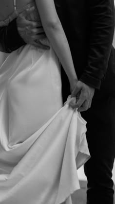 the bride and groom are holding each other's wedding dress while they stand close together