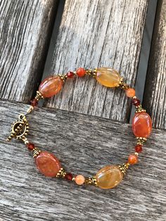 Red Agate is a gem that resembles the colors of the warmest sunsets... alluring and vivid, this bracelet is designed to entice thoughts of the setting sun.  The oval beads showcase the natural color striations and unique patterns found in Agate.  Swarovski crystals in tonal hues compliment the unique, glowing shades of red, orange and yellow these gems display.  Goldfilled beads and gold plated pewter accents continue the warm feeling of this bracelet which closes with a beaded toggle clasp.  As the bracelet moves on your wrist, it will catch your eye as each gem radiates a sense of passion for life! For those interested in the metaphysical properties of gems, Red Agate is thought to "strengthen your inner balance" and "keep negative energy away from the wearer"... Red Agate : Elegant Orange Gemstone Beaded Bracelet, Elegant Orange Beaded Bracelets With Gemstones, Elegant Orange Beaded Bracelet With Natural Stones, Elegant Orange Gemstone Beaded Bracelets, Elegant Orange Bracelet, Handmade Orange Agate Beaded Bracelets, Spiritual Carnelian Orange Bracelets, Bohemian Carnelian Bracelet In Orange, Spiritual Orange Carnelian Bracelets