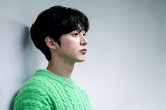 a young man in a green sweater leaning against a wall with his head turned to the side