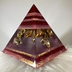 a triangle shaped object with gold elephants on it's sides, sitting on top of white fur