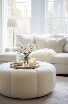 a living room filled with white furniture and flowers on top of a round coffee table