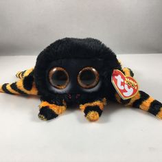 a black and yellow stuffed spider with big eyes on it's head, sitting on a white surface