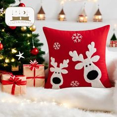 a red pillow with reindeers on it next to a christmas tree