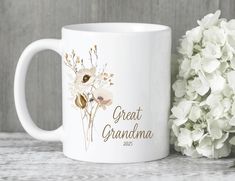 a white coffee mug with the words great grandma printed on it next to some flowers