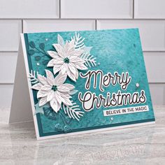 a merry christmas card with white flowers on blue and green cardstocked in silver foil