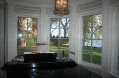 a room with three windows and a piano in the corner by the window is a lake