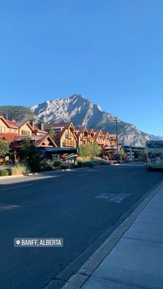 an empty street in front of some mountains with houses on each side and cars parked along the road