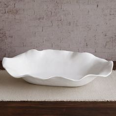 a large white bowl sitting on top of a table next to a wooden tablecloth