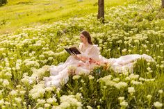 a woman sitting in the middle of a field with flowers on her lap reading a book