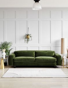 a living room with white walls and green couch in the center, surrounded by two gold vases