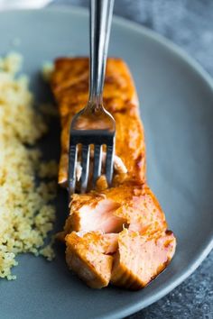 a fork is stuck into some meat on a plate with rice and broccoli