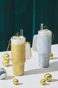 two coffee mugs decorated with gold and silver glitter, next to some christmas ornaments