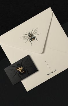 a black and white envelope with a gold bee on it's side, next to a card