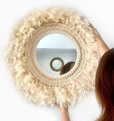 a woman is looking at her reflection in a mirror with some feathers on the wall