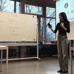 a woman standing in front of a whiteboard with writing on it and holding a cell phone