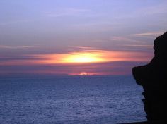 the sun is setting over the ocean and rocks