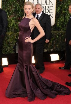 a woman in a purple gown standing on the red carpet at an event with other people behind her