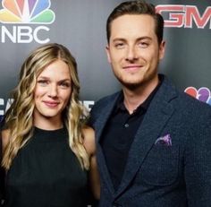 two people standing next to each other in front of a red carpet with the nbc logo on it