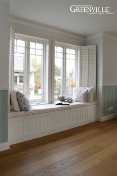 a window seat with pillows on it in front of two windows and a wooden floor