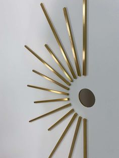 a clock made out of gold sticks on top of a white wall with a circular hole in the middle