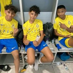 three young men sitting in lockers wearing yellow shirts and blue shorts