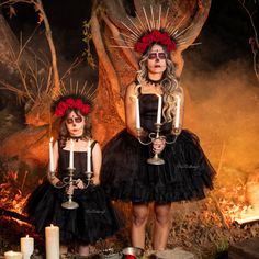 two women dressed in black and red are holding candles