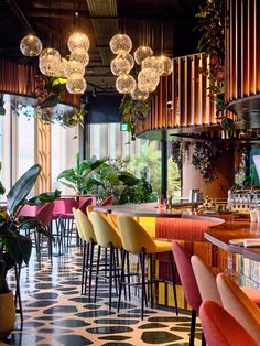 the interior of a restaurant with many colorful chairs and lights hanging from the ceiling, along with potted plants