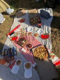 an outdoor picnic with pizza, drinks and snacks on the blanket in the grass outside