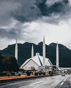 a very tall church sitting on the side of a road under a cloudy sky with mountains in the background