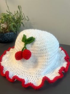 a crocheted hat with two strawberries on the brim, sitting next to a potted plant