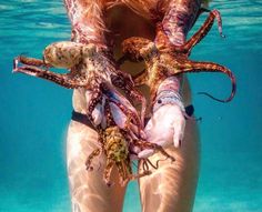 a woman holding an octopus in her hands under the water's surface, with it's skin exposed