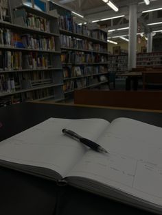 an open book with a pen sitting on top of it in front of a library full of books