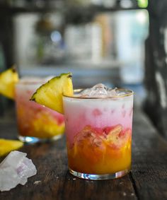 two glasses filled with drinks sitting on top of a wooden table next to pineapple slices