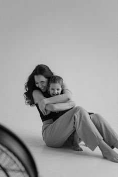 a woman sitting on the ground holding a child with her arms wrapped around her neck