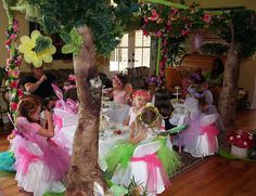 a group of children dressed in fairy costumes sitting at a table with flowers on it