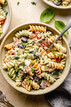 two bowls filled with pasta salad on top of a table next to utensils