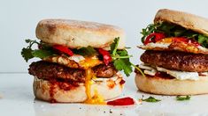 two burgers with meat, cheese and vegetables on them are sitting on a marble surface