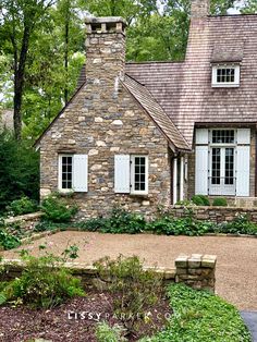 a stone house with white shutters on the front and side windows is surrounded by greenery