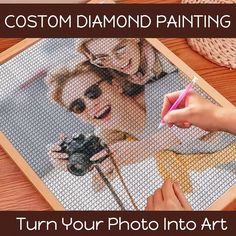 a woman holding a pink pen in front of a photo on a wooden table with text that reads, custom diamond painting turn your photo into art